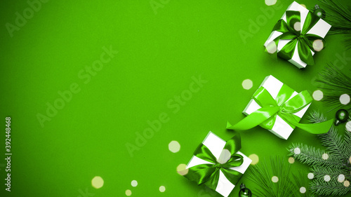 Gifts background. White gift box with emerald color ribbon, New Year balls and sparkling lights in Christmas composition on dark green background for greeting card. Flat lay, top view, copy space.