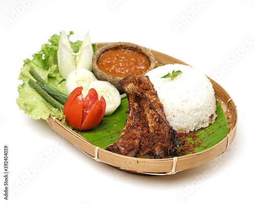 Sambel iwak pe (stingray) or penyet. indonesian culinary. tingrays with a splash of Sambal and side dish such as cucumber slices, fried eggplant, tempeh , tofu serve with sambal on stone plate. photo