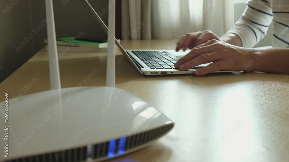 Selective focus at men hand and keyboard. Blurred internet router on working table with man typing on computer laptop. Fast and high speed internet connection from fiber line with LAN cable connection