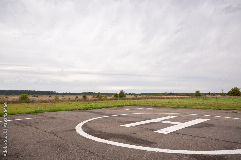 Private helipad after rain. An asphalt helipad against the backdrop of a green field and a cloudy evening sky.