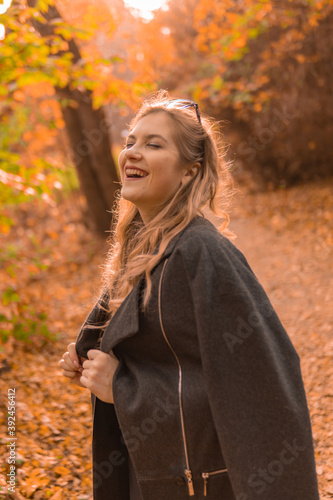 Happy girl in a black cloak stands in chameleon glasses in autumn. Yellow forest  green grass  blonde. looking at camera