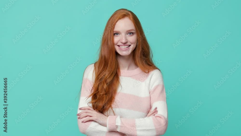 Smiling pretty ginger redhead young girl wearing white pink sweater posing isolated on blue turquoise color background in studio. People lifestyle concept. Looking at camera holding hands crossed Smiling pretty ginger redhead young girl wearing white pink sweater posing isolated on blue turquoise color background in studio. People lifestyle concept. Looking at camera holding hands crossed
