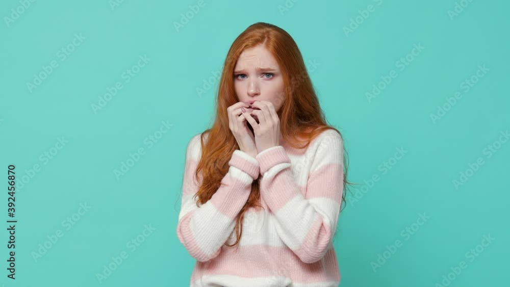Shocked worried scared ginger redhead young girl wearing white pink sweater posing isolated on blue turquoise color background in studio. People lifestyle concept. Looking camera covering with hands Shocked worried scared ginger redhead young girl wearing white pink sweater posing isolated on blue turquoise color background in studio. People lifestyle concept. Looking camera covering with hands