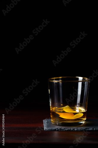 Whiskey with lemon zest served on slate plate. Dark red wooden table, high resolution
