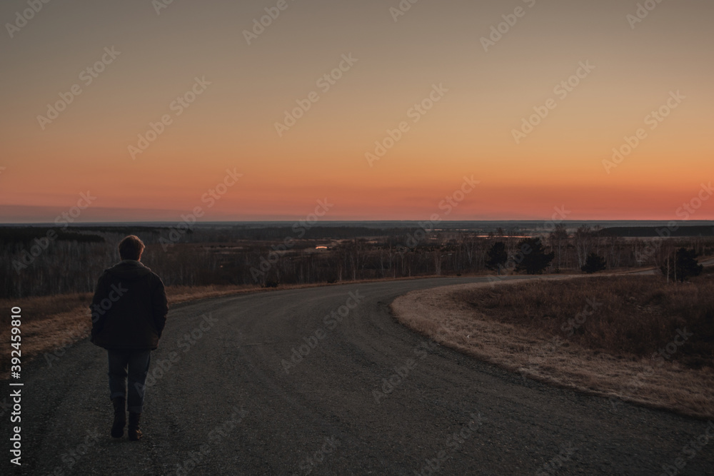 Man walks along turning paved road on hill at sunset. Copy space