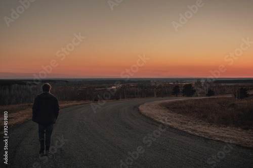 Man walks along turning paved road on hill at sunset. Copy space