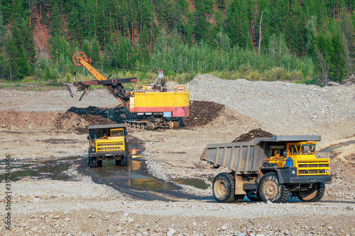    Dump truck and excavator at work. Mining.
Excavator loads mountain soil into the body of a dump truck