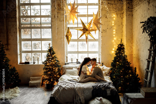 Tender couple with garland sit near the Christmas tree at home, cuddling, loving husband with lovely wife spend winter holidays, enjoy togetherness, New Year celebration concept