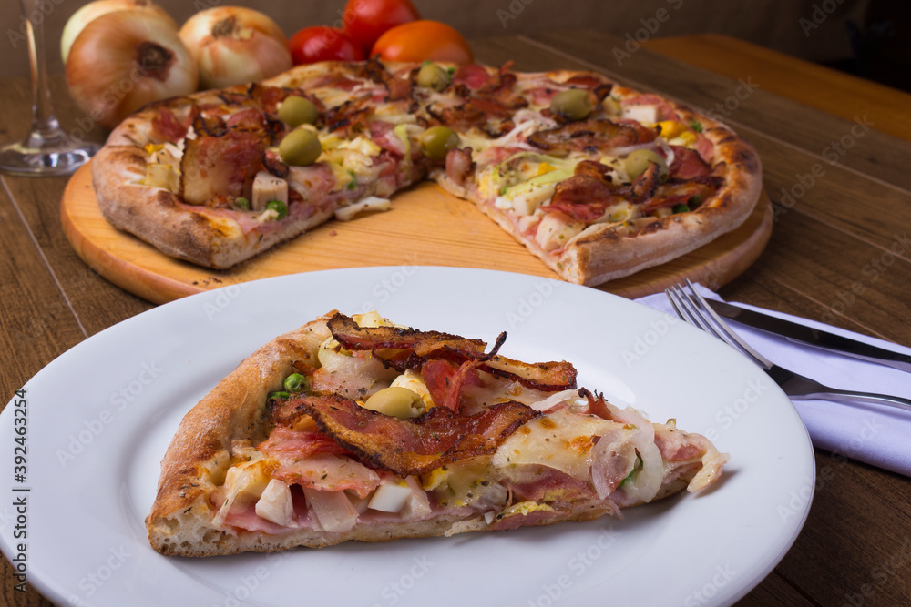 Portuguese Pizza slice made with ham, pea egg, heart of palm, pepperoni, onion and mozzarella and bacon. Served on the plate with sliced ​​pizza in the background. Close-up photo for pizzerias.