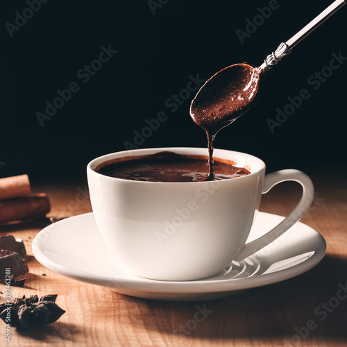 Liquid hot chocolate flow from spoon into cup on a wooden table with dark background, close-up view