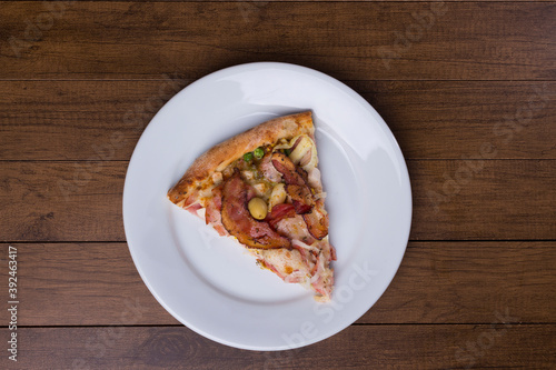 Pizza slice served on the plate. Portuguese pizza made with ham, pea egg, heart of palm, pepperoni, onion and mozzarella and bacon. Top shot with elements aligned to the center of the image.
