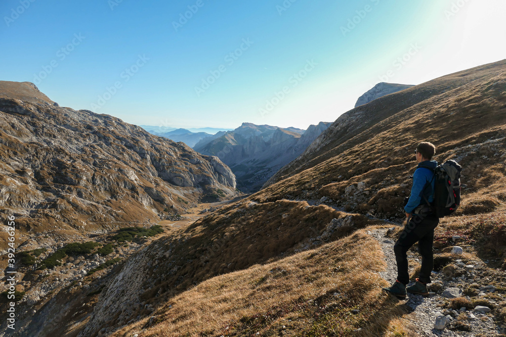 A man hiking in Hochschwab in Austrian Alps. Steep mountain chain in front of him. Massive Alps. The grass hast turned golden. Autumn vibes in the mountains. Idyllic landscape. Freedom and wilderness