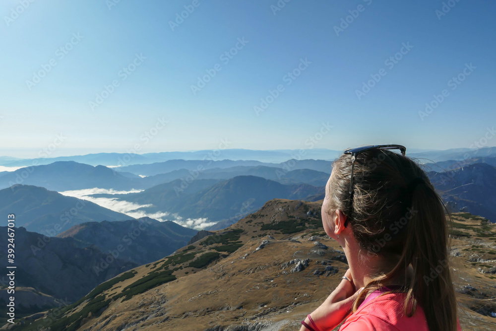 A woman enjoying the view on valley shrouded in fog from top of a mountain in Hochschwab region in Austrian Alps. The flora overgrowing the slopes is turning golden. Freedom. Mysterious landscape