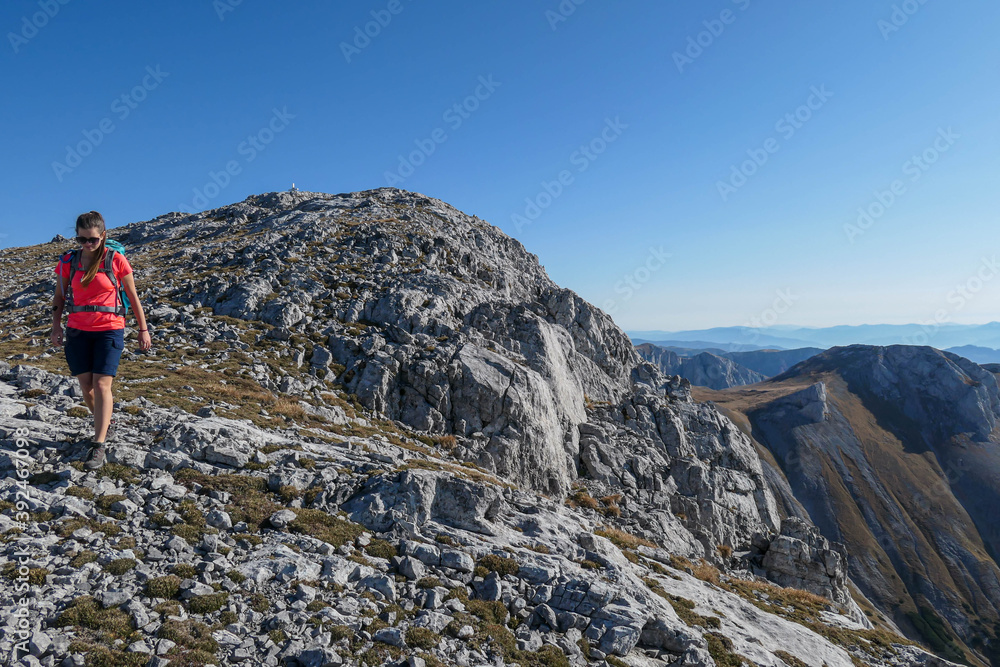 A woman hiking on a mountain ridge in Hochschwab region in Austrian Alps. Steep and stony slopes. Massive Alps. Autumn vibes in the mountains. Idyllic landscape. Freedom and wilderness