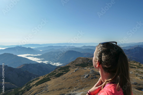 A woman enjoying the view on valley shrouded in fog from top of a mountain in Hochschwab region in Austrian Alps. The flora overgrowing the slopes is turning golden. Freedom. Mysterious landscape © Chris