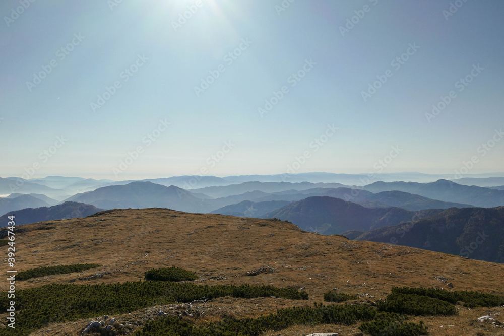 Fototapeta premium A panoramic view on the plain on top of a mountain in Hochschwab region in Austrian Alps. The flora overgrowing the slopes is turning golden. The valley is shrouded in fog. Mysterious landscape