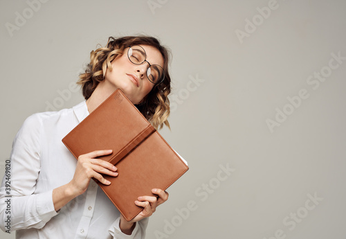 Woman with brown notepad on a gray background and glasses on her face © SHOTPRIME STUDIO