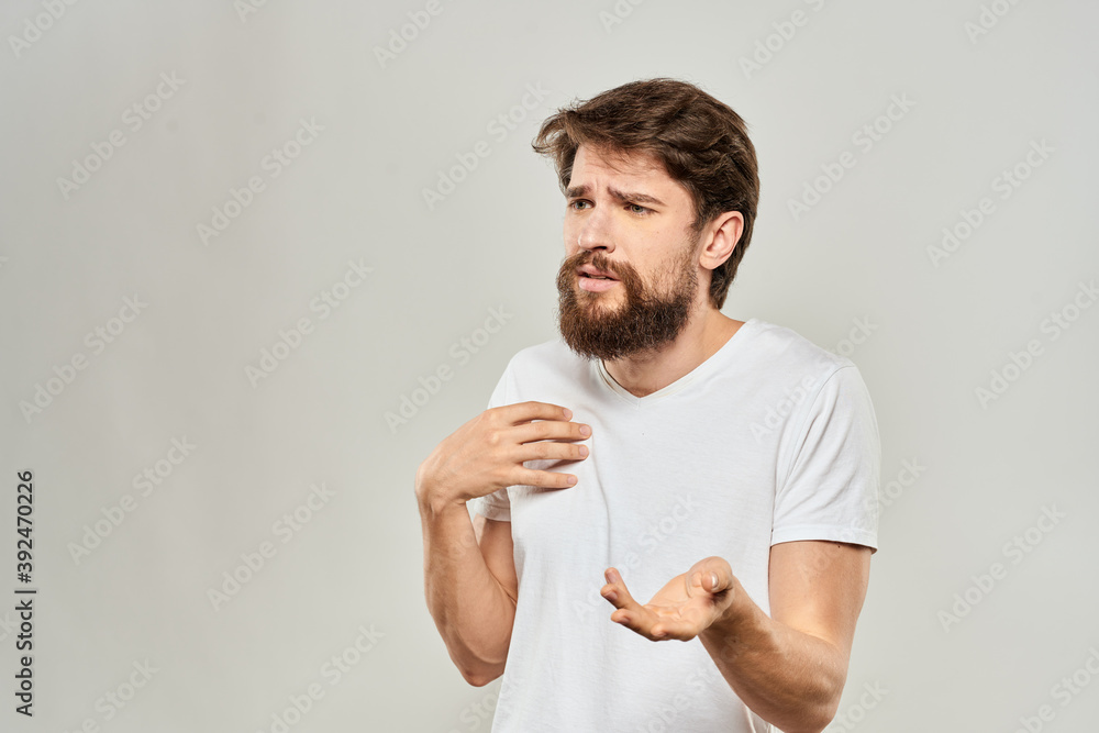 A man in a white t-shirt with a beard emotions displeased facial expression light background A man in a white t-shirt with a beard emotions displeased facial expression light background