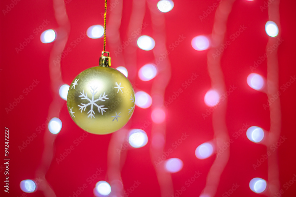 Fototapeta premium Yellow Christmas ball on a background of a glowing garland. Christmas decorations on a red background. Holiday decorations. Christmas concept. 