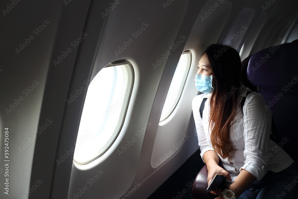Fototapeta premium Asian woman tourist on airplane, medical protective sterile mask on his face traveling. Pandemic covid-19. Safety in public transport.Coronavirus flu virus travel concept