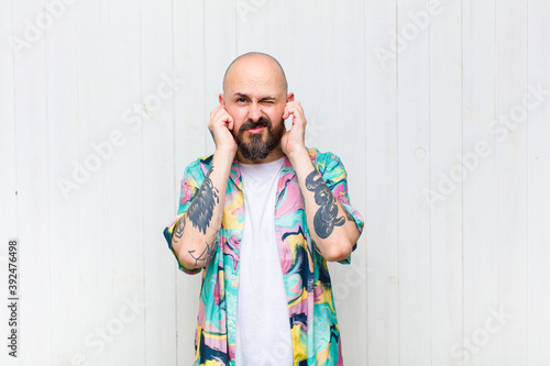 Фотография bald man looking angry, stressed and annoyed, covering both ears to a deafening