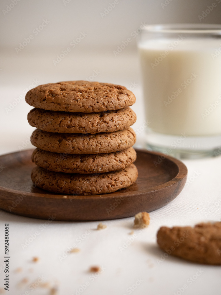 Oatmeal cookies in a wooden plate and a glass with milk on a white background Oatmeal cookies in a wooden plate and a glass with milk on a white background