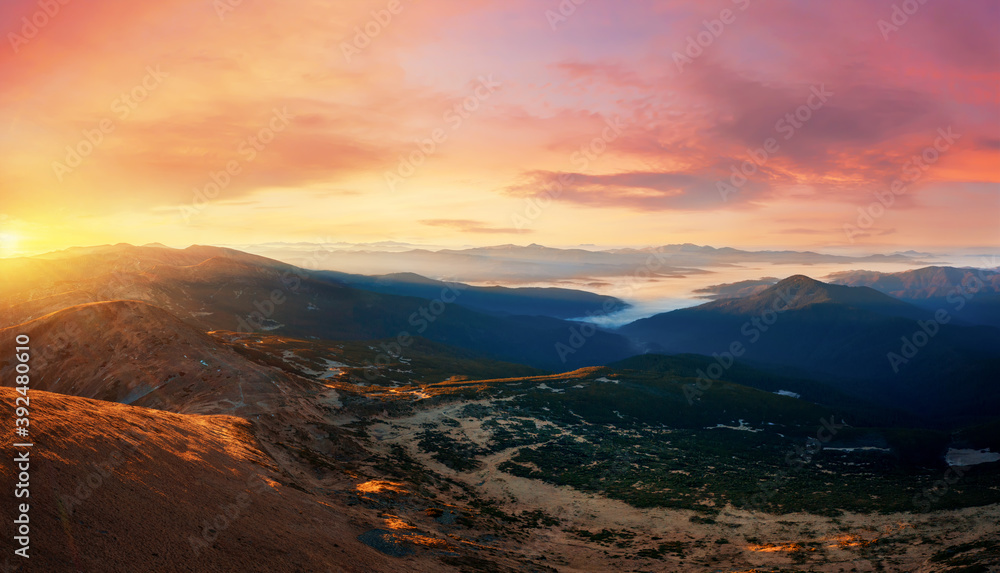 Sunset panorama in a mountain valley with low clouds.