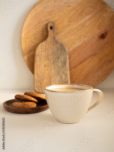 Oatmeal cookies in a wooden plate and a cup of coffee with milk on a white background