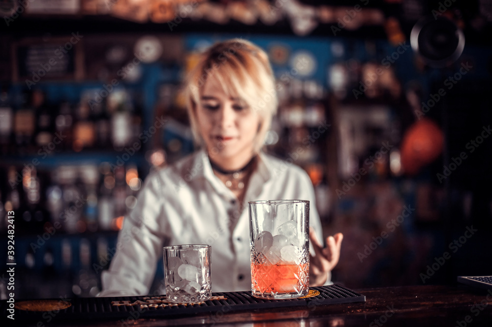 Focused girl tapster intensely finishes his creation while standing near the bar counter in pub