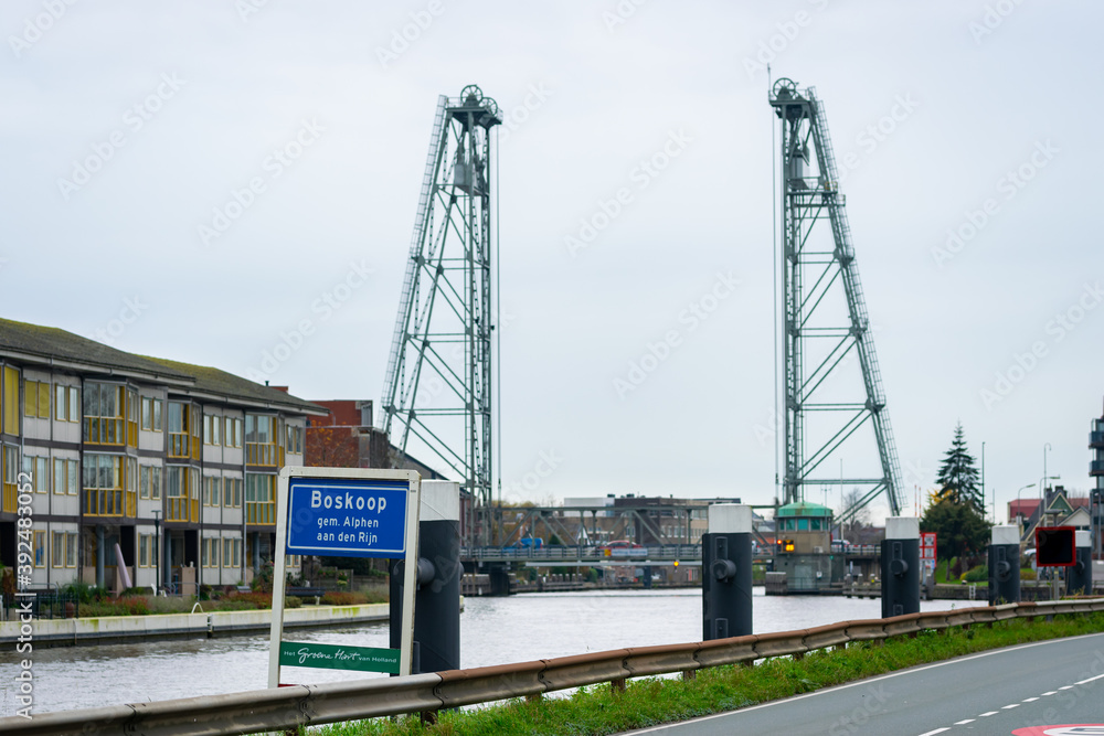 Place name sign of the village of Boskoop (municipality of Alphen aan den Rijn) in The Netherlands. In the defocused background the lift bridge over canalized river Gouwe.