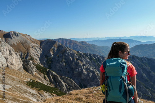 A woman with big blue backpack enjoying the view on valley from top of a mountain in Hochschwab region in Austrian Alps. The flora overgrowing the slopes is turning golden. Freedom. She is happy