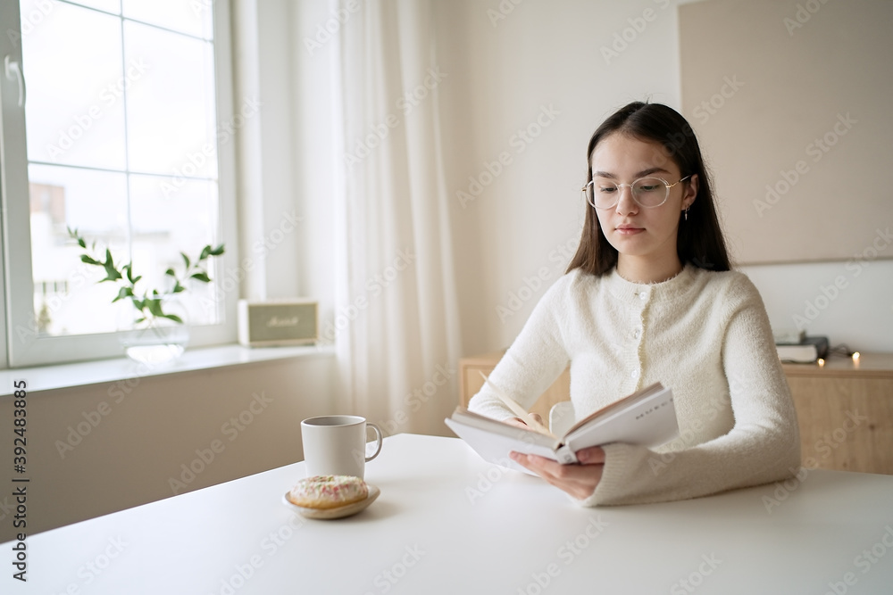 Pretty teenage girl reading book and drinking coffee at home Pretty teenage girl reading book and drinking coffee at home
