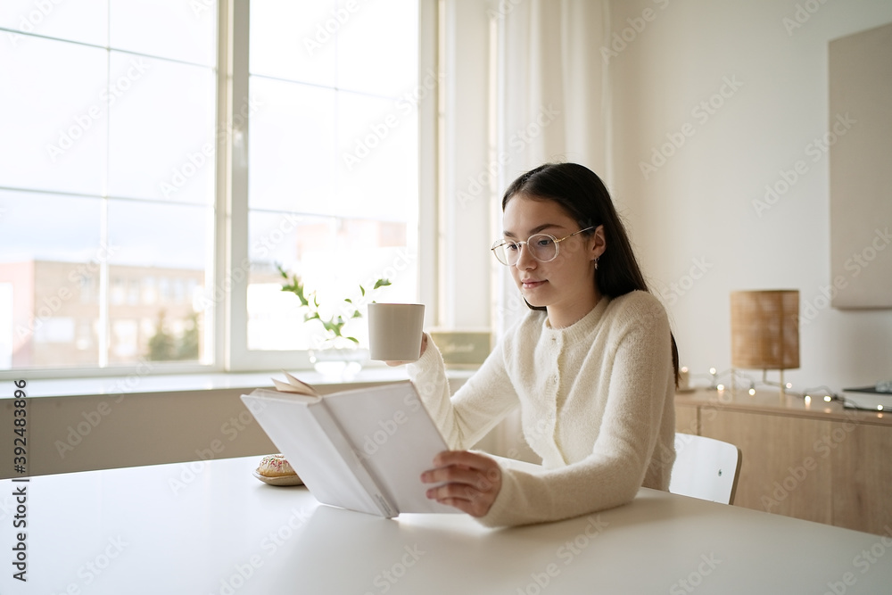 Pretty teenage girl reading book and drinking coffee at home Pretty teenage girl reading book and drinking coffee at home