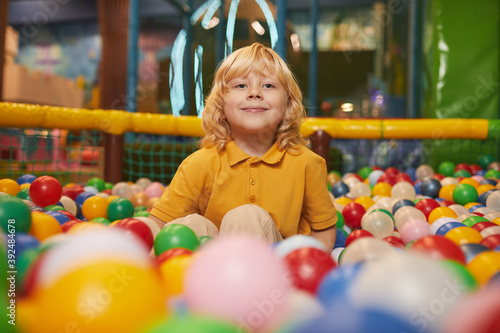 Portrait of little boy with blond hair smiling at camera while sitting in pool with colored balls