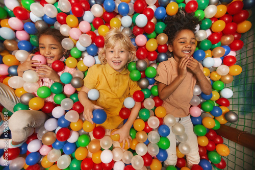 High angle view of group of happy children smiling at camera while lying among colored balls in the pool