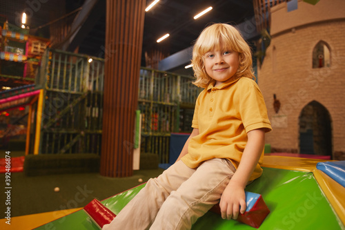 Portrait of cute little boy with blond hair looking at camera while playing in entertainment park
