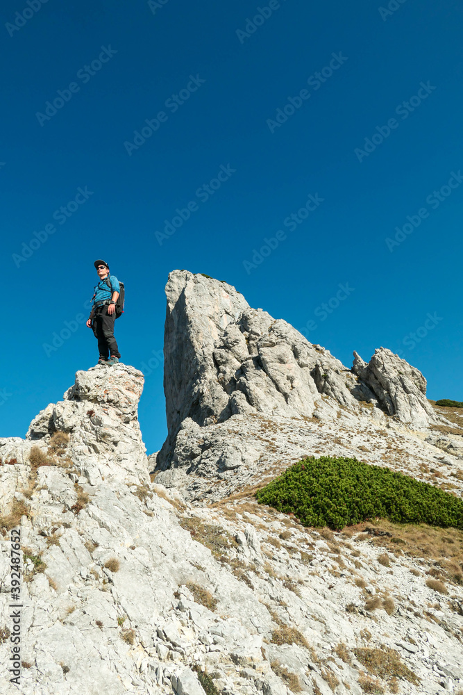 A man standing on top of a sharp, pointy boulder in Hochschwab region, Austrian Alps. The steep mountain wall in front look very dangerous. High mountaineering. Autumn vibes. Adventure and freedom
