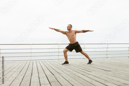 Muscular man with a naked torso practice hatha yoga, balancing pose at beach. Healthy lifestyle concept