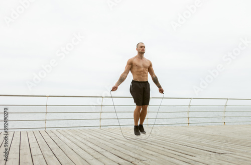 Embossed muscular man exercising with skipping rope on the beach