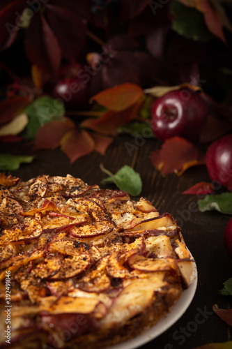 Delicious sweet pie with red apples, apple pie sprinkled with cocoa on a wooden background, rustic style, background of red leaves of grapes and ripe fruits