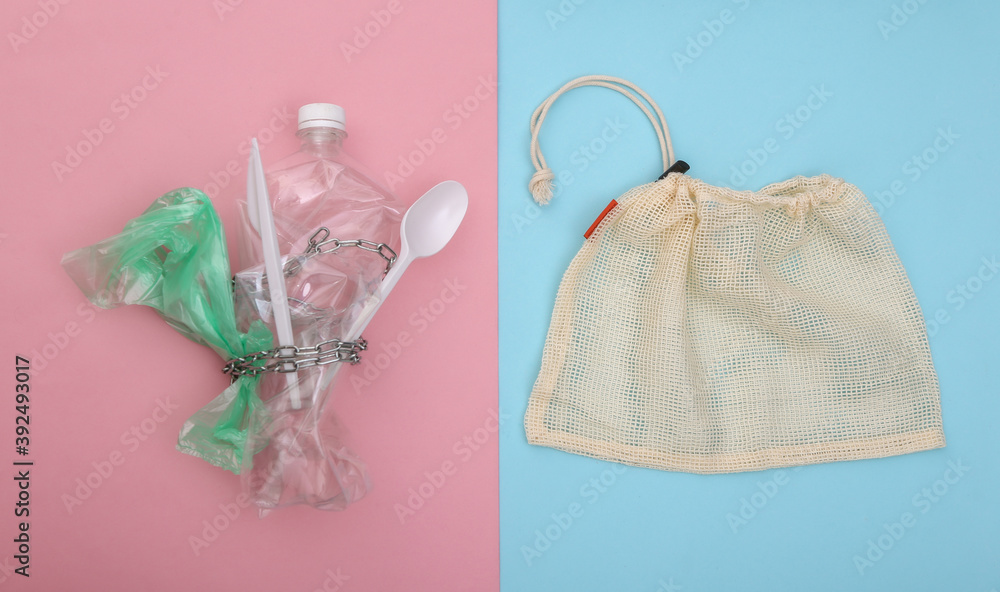 Eco bag and plastic products wrapped in a steel chain on a blue-pink pastel background. Top view Eco bag and plastic products wrapped in a steel chain on a blue-pink pastel background. Top view