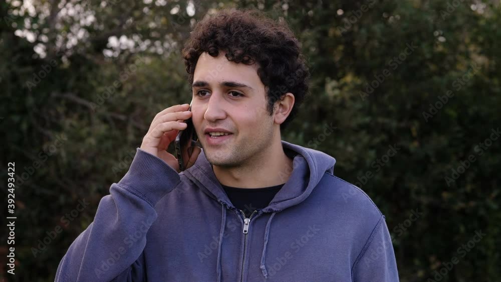 technology, conversation - young relaxed man talks on his mobile at park