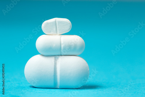 Three white  tablets of different sizes on blue   dosage