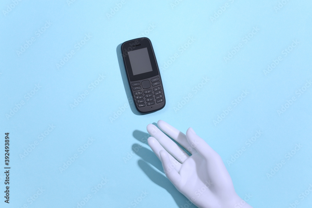 Mannequin's hand holds a push-button telephone on blue background. Top view