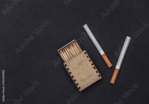 Cigarettes and box of matches on black background. Top view