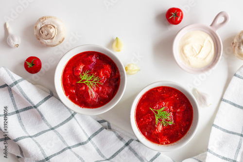 Top view of the traditional Ukrainian borscht or soup with beets, potatoes, tomatoes, meat in bowls on a white background. Top view, copy space.