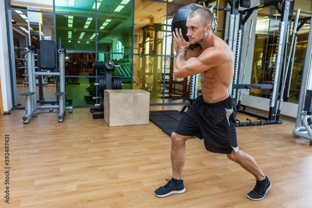 Muscular fitness man exercising with medicine ball on his shoulder in the gym. Cross training