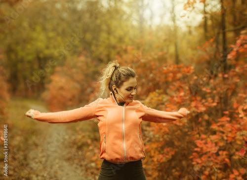 Fototapeta Naklejka Na Ścianę i Meble -  Young attractive sport woman in sportswear doing stretching exercise for hand in autumn forest with reddened leaves of trees. Warm up before training. Healthy lifestyle concept