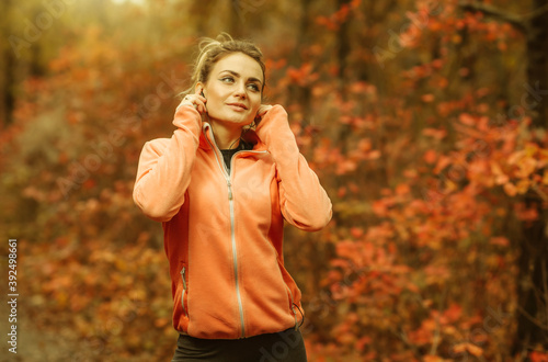 Young fit woman in sportswear listening to music with headphones on forest path with reddened leaves. Healthy lifestyle concept
