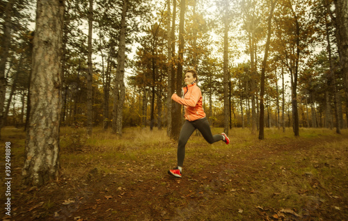 Jogging through the autumn forest. Young fit woman in sportswear runs along forest path. Healthy lifestyle concept